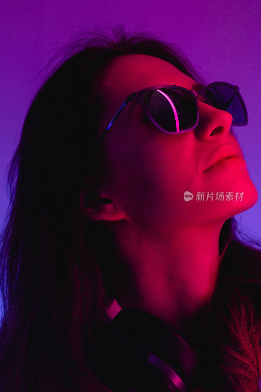 Female portrait in neon light. Fashion woman in purple color. Vibrant background at the studio. Futuristic concept. Girl wear sunglasses and hoodie with bluetooth wireless headphones